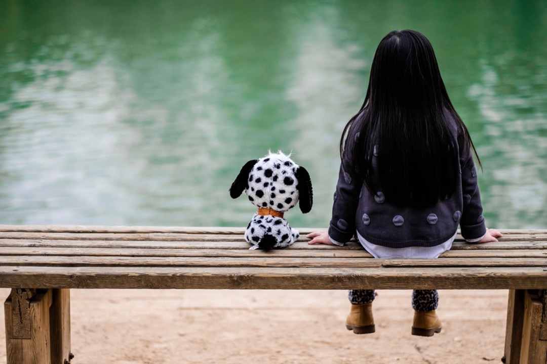 Foto van een meisje op een bank met een knuffelhondje ernaast