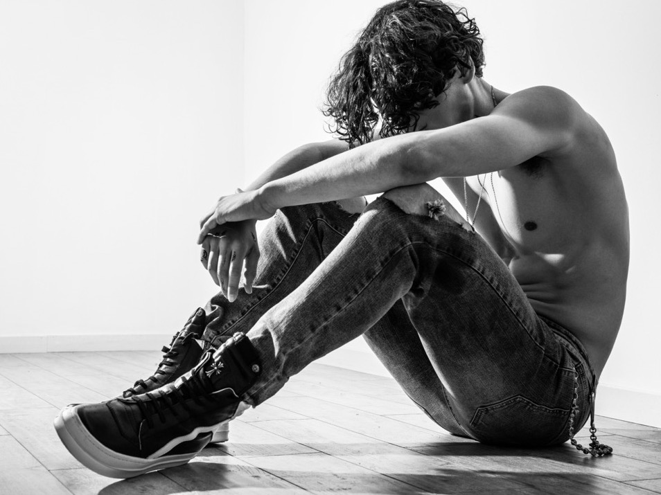 Zwart/wit foto van een sombere zittende jongeman in spijkerbroek